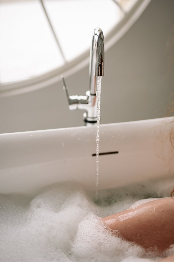 A serene bathtub filled with bubbles and flowing water from a chrome faucet indoors.